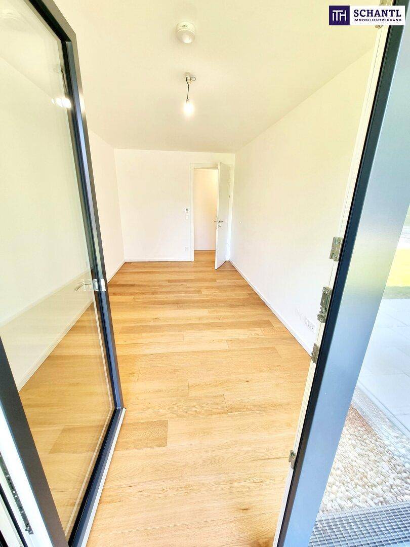 Leeres Zimmer mit Holzboden und einer großen Glastür, die viel Tageslicht hereinlässt.