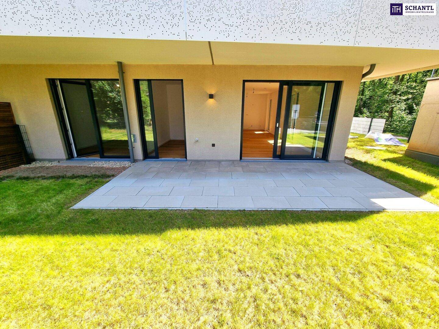 Eine gepflasterte Terrasse grenzt an eine grüne Rasenfläche vor dem modernen Gebäude.