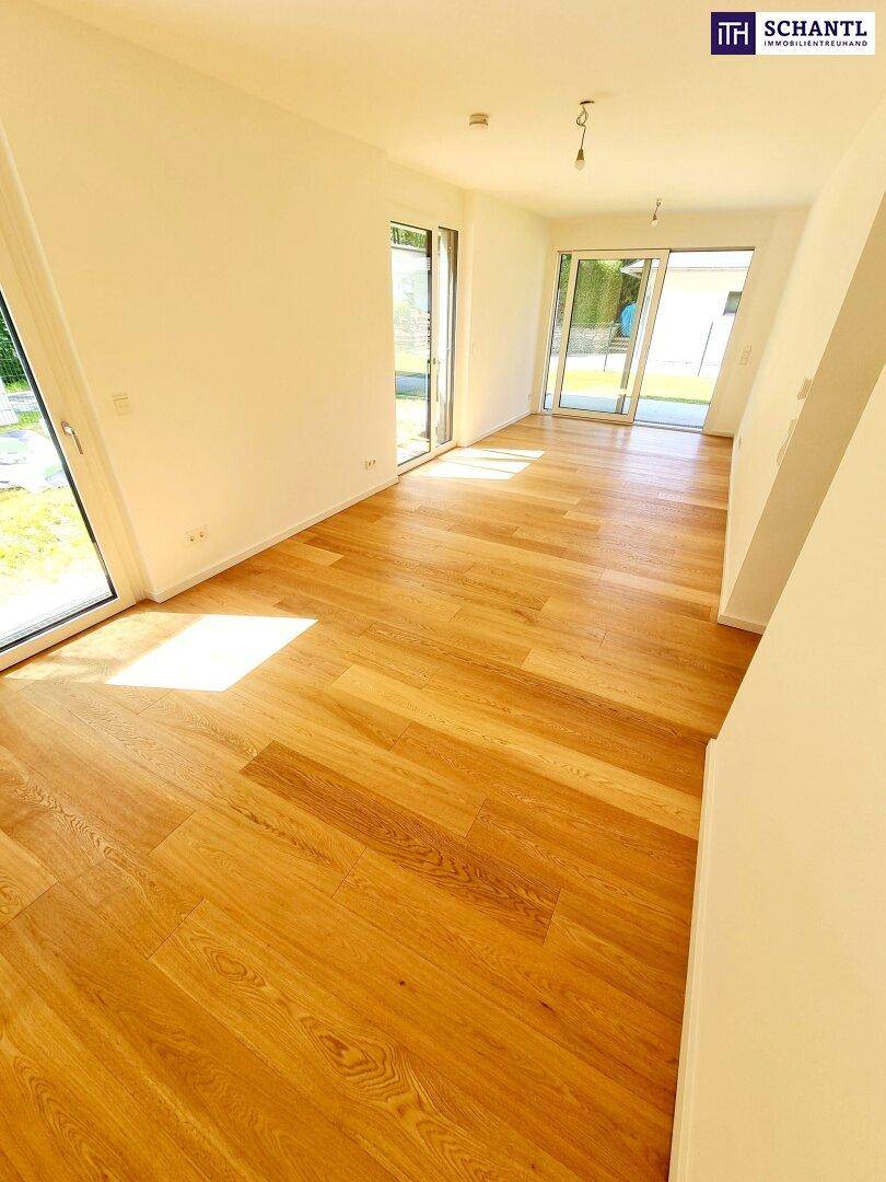 Helles, leeres Zimmer mit Holzboden und großen Glastüren, die Zugang zum Garten bieten.