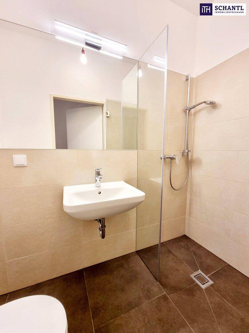 Helles Badezimmer mit modernem Waschbecken, großer Spiegelfläche und ebenerdiger Dusche.