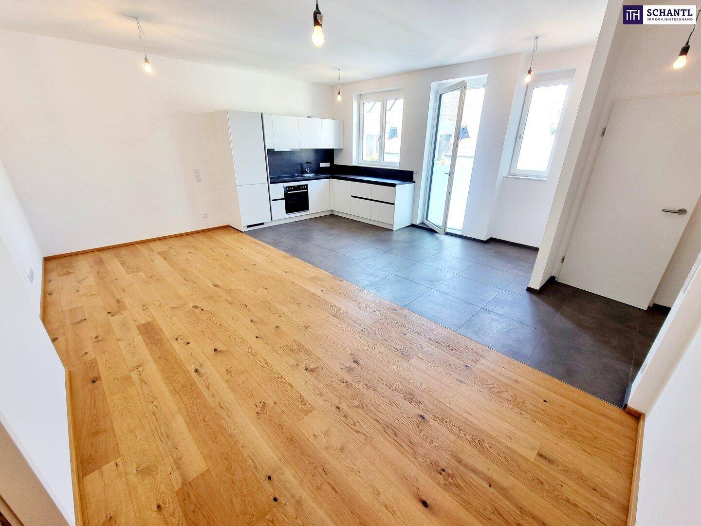Heller offener Wohn-Essbereich mit moderner Einbauküche, Holzboden und Zugang nach draußen.