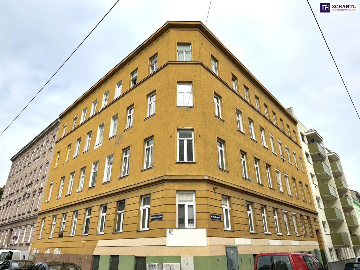 Mehrstöckiges Eckgebäude mit gelb-orangefarbener Fassade und vielen Fenstern unter bewölktem Himmel.