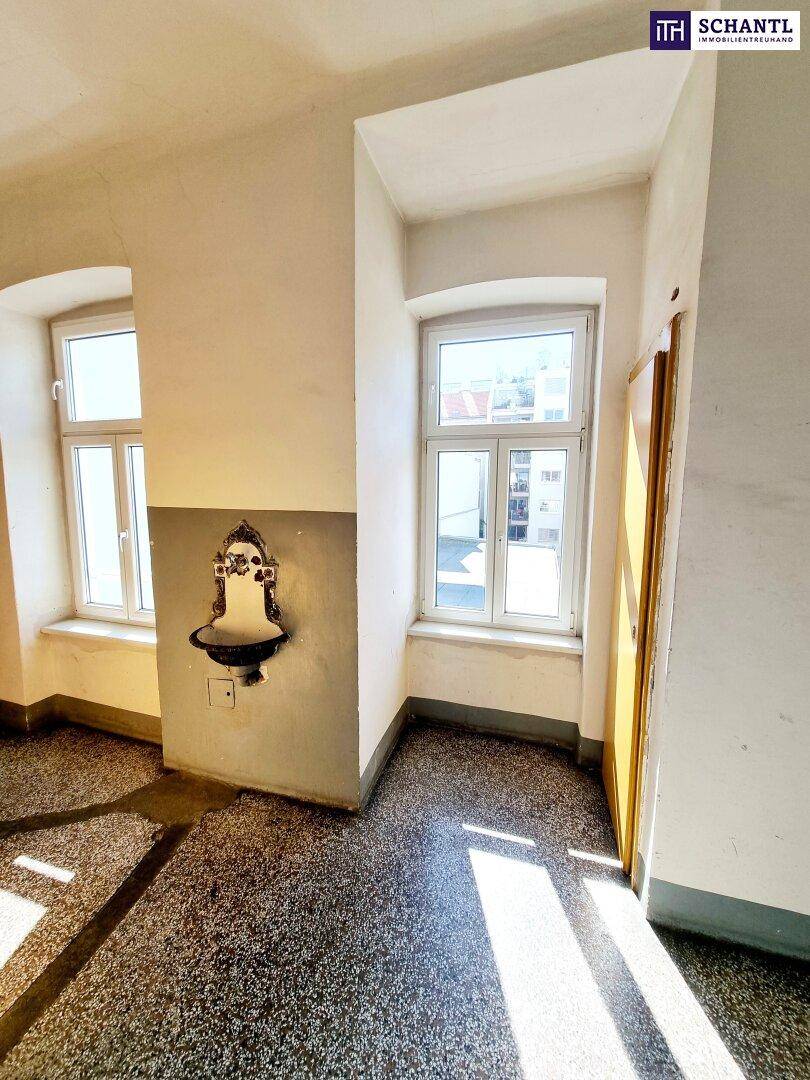 Heller Flur mit Terrazzoboden, hohen Fenstern und einem dekorativen Wandbrunnen.