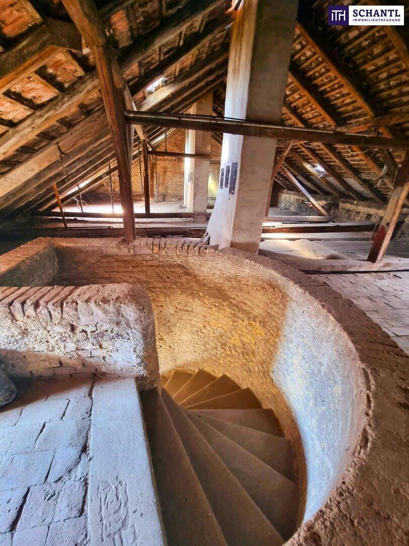 Unausgebauter Dachboden mit sichtbaren Holzbalken und einer Wendeltreppe.