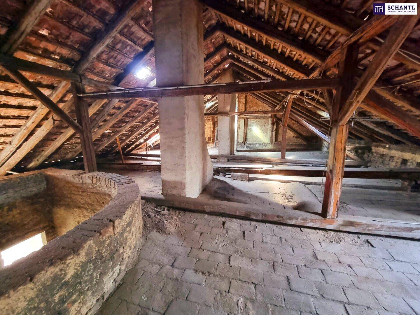 Geräumiger, unausgebauter Dachboden mit sichtbarer Holzkonstruktion und Ziegelboden.