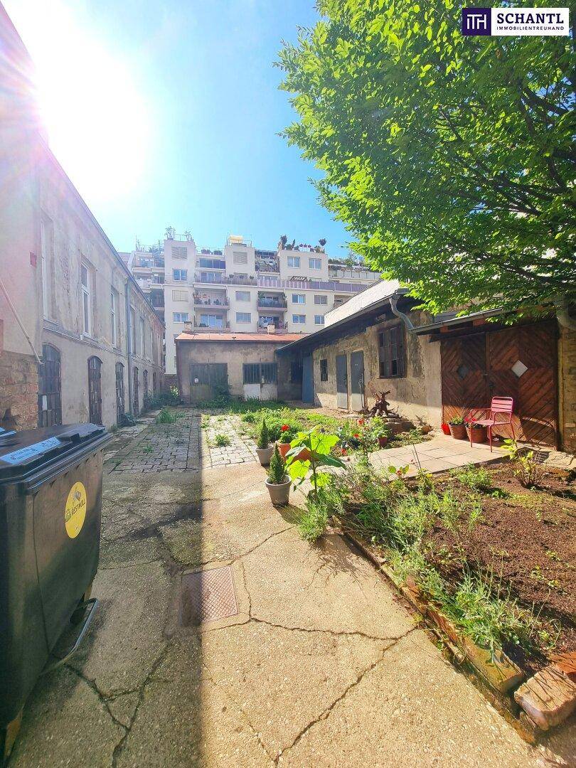 Sonniger Innenhof mit alten Gebäuden, Pflanzen und einem gepflasterten Weg.
