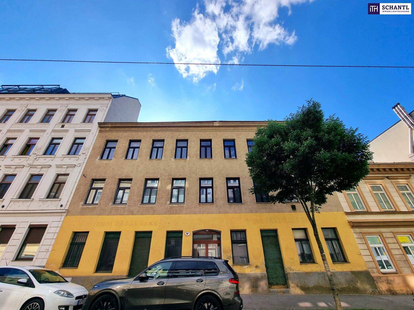 Historische Gebäudefassade mit gelber und grauer Farbgebung an einer Stadtstraße.
