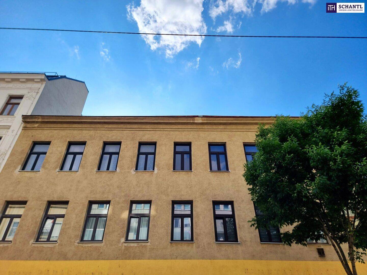 Historische Gebäudefassade mit gelber und grauer Farbgebung unter blauem Himmel.