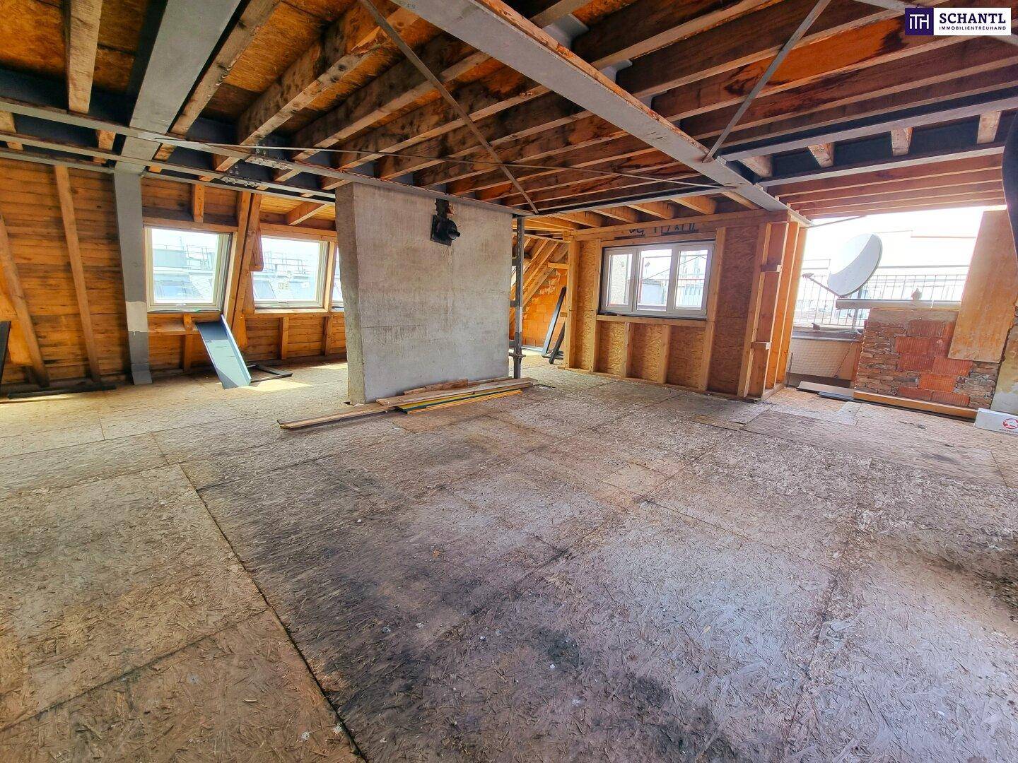 Großer, unfertiger Dachbodenraum mit Holzbalken und Fenstern, ideal für zukünftige Wohnnutzung.