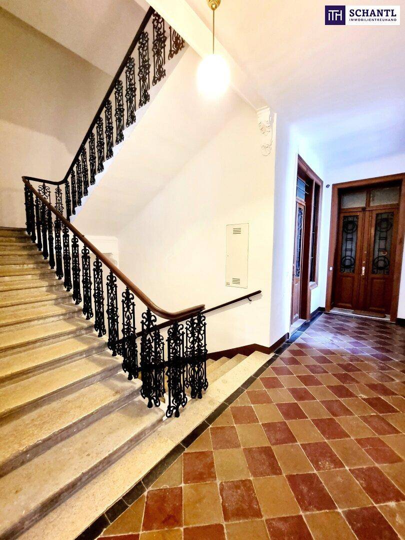 Elegantes Treppenhaus mit schmiedeeisernem Geländer und gemusterten Fliesen im Eingangsbereich eines Altbaus.