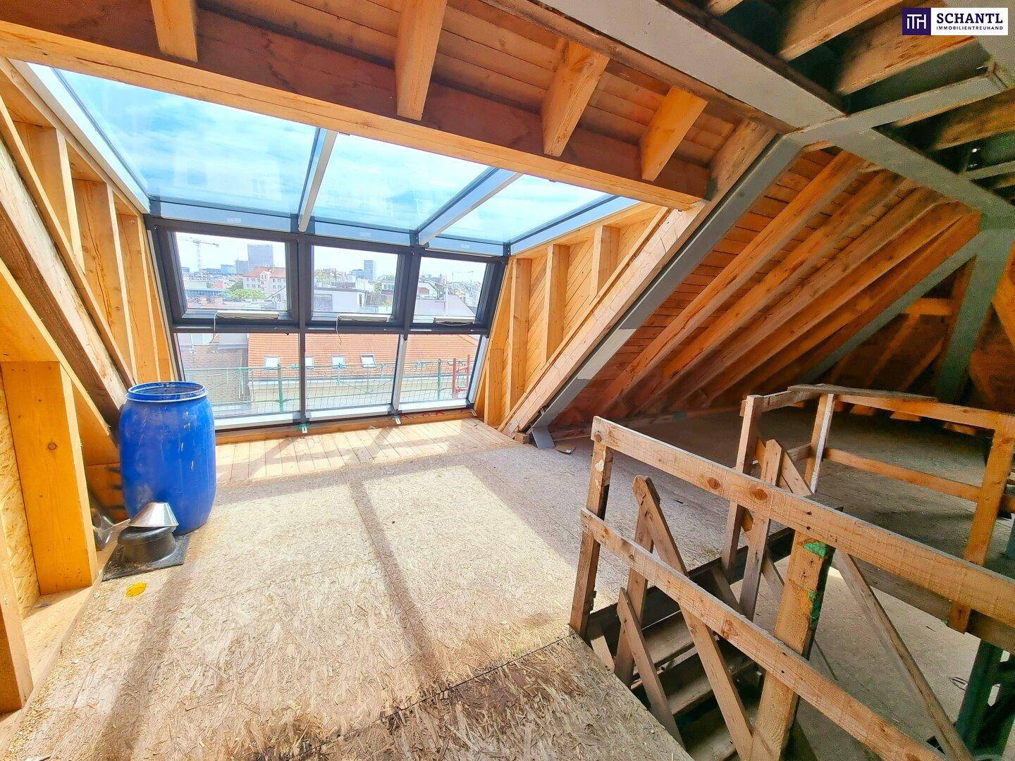 Helles Dachgeschoss mit großer Glasfront, Stadtblick und Holztreppe, ideal für den Ausbau.
