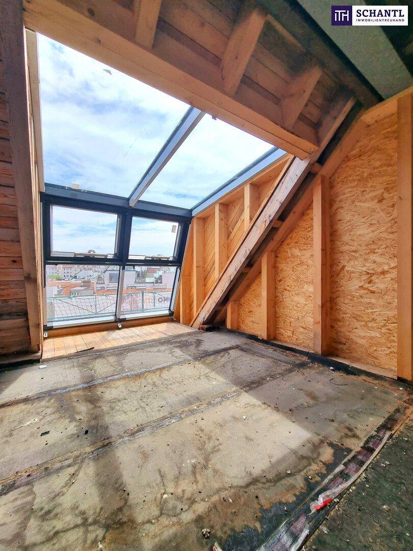 Rohbau-Innenraum mit großen Fenstern, Dachfenster und sichtbaren Holzbalken unter dem Dach.