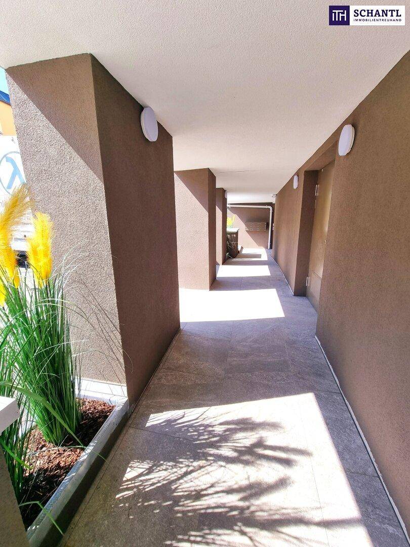 Überdachter Außenflur mit brauner Fassade und modernen Bodenfliesen.