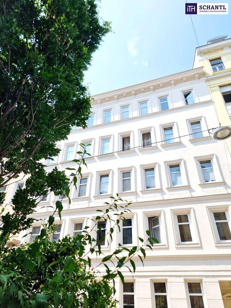 Klassische Fassade eines Mehrfamilienhauses mit vielen Fenstern, umgeben von grünen Bäumen.