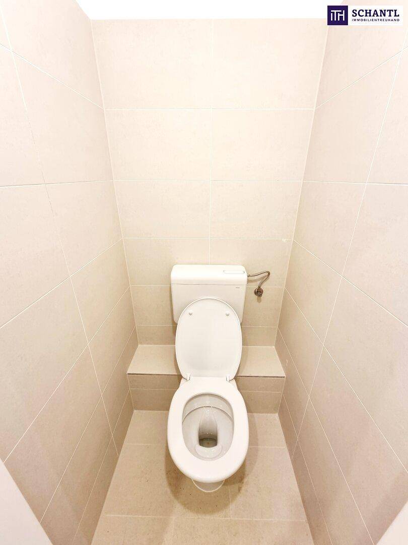 Separates WC mit wandmontierter Toilette und hellen Fliesen an Wänden und Boden.