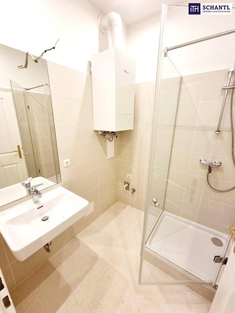 Modernes Badezimmer mit Duschkabine, Waschbecken und hellen Fliesen, inklusive Warmwasserbereiter.