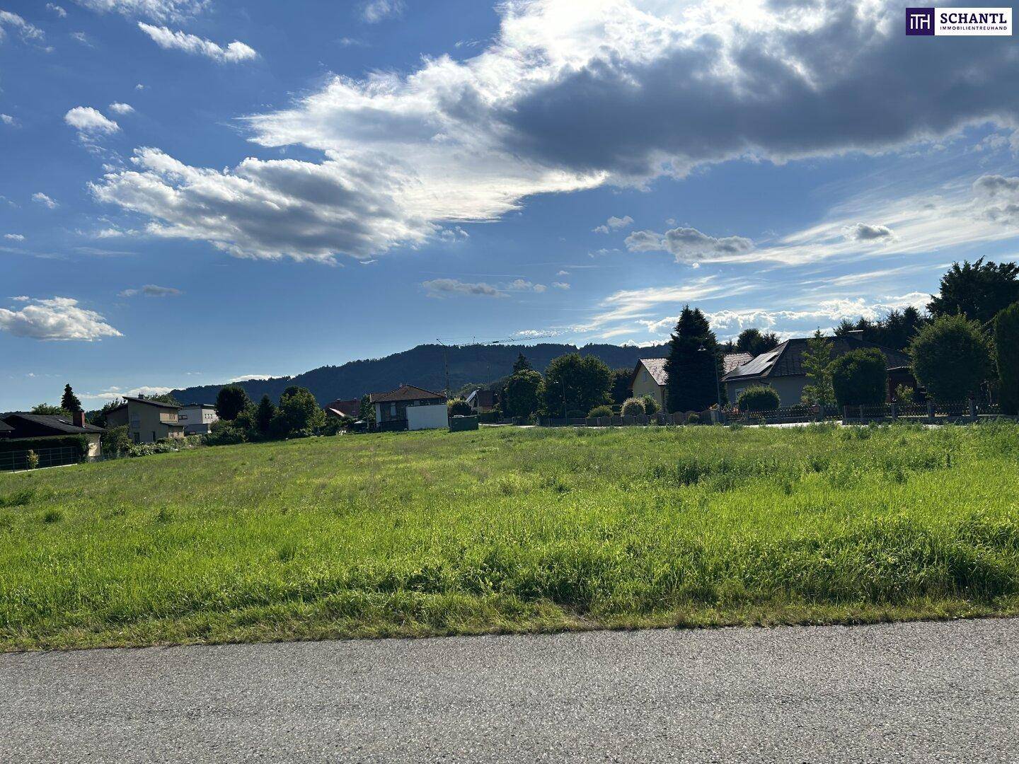 Grünes Baugrundstück mit Blick auf die hügelige Landschaft und die umliegenden Wohnhäuser.