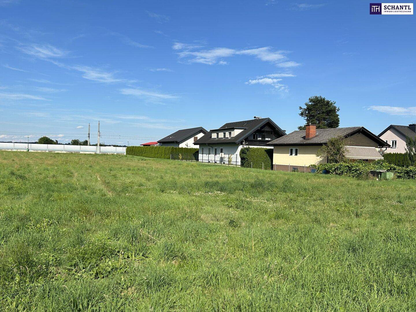 Weitläufiges Wiesengrundstück mit angrenzenden Einfamilienhäusern unter klarem blauem Himmel.