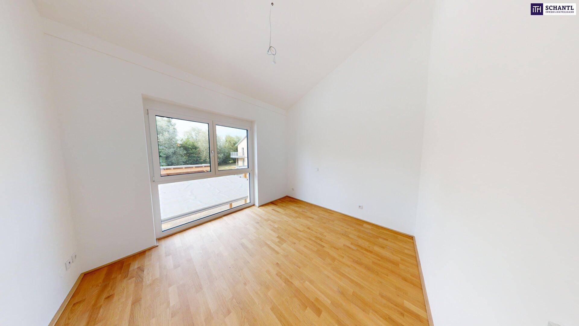 Geräumiges Zimmer mit Parkettboden und breitem Fenster mit Blick ins Grüne.