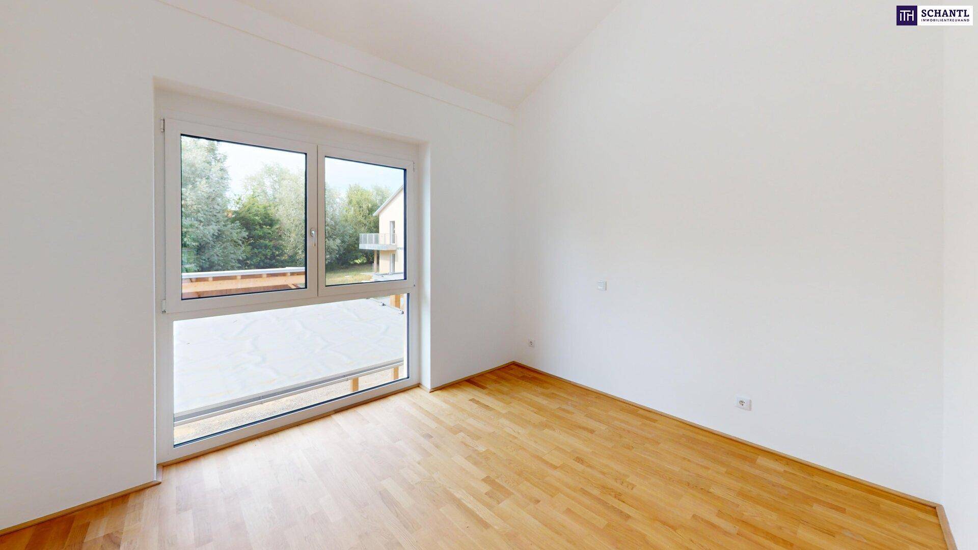 Geräumiges Zimmer mit Parkettboden und großem Fenster, das einen Blick nach draußen ermöglicht.
