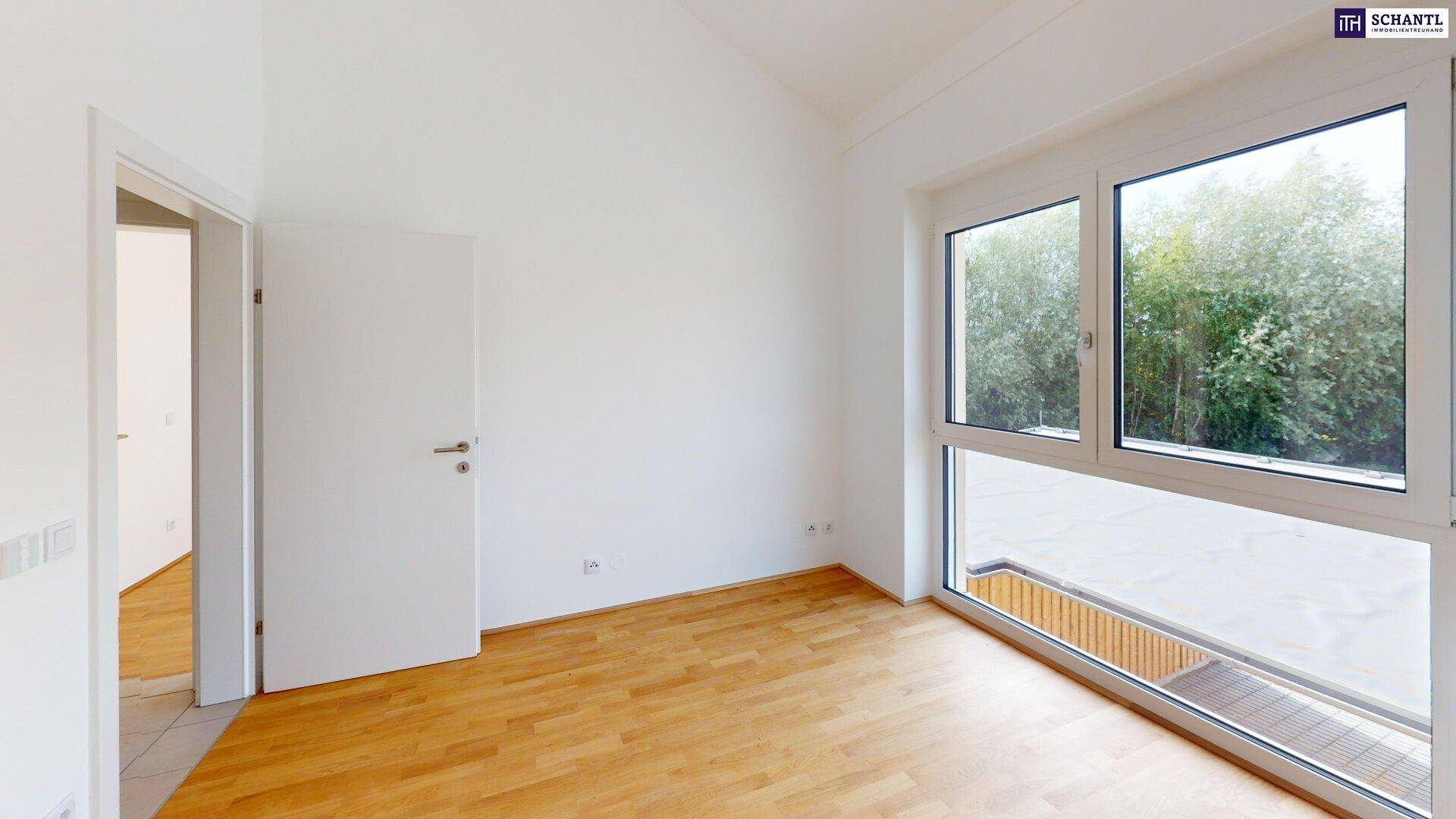 Helles Zimmer mit Parkettboden und Fensterfront, die viel Tageslicht hereinlässt und eine angenehme Atmosphäre schafft.