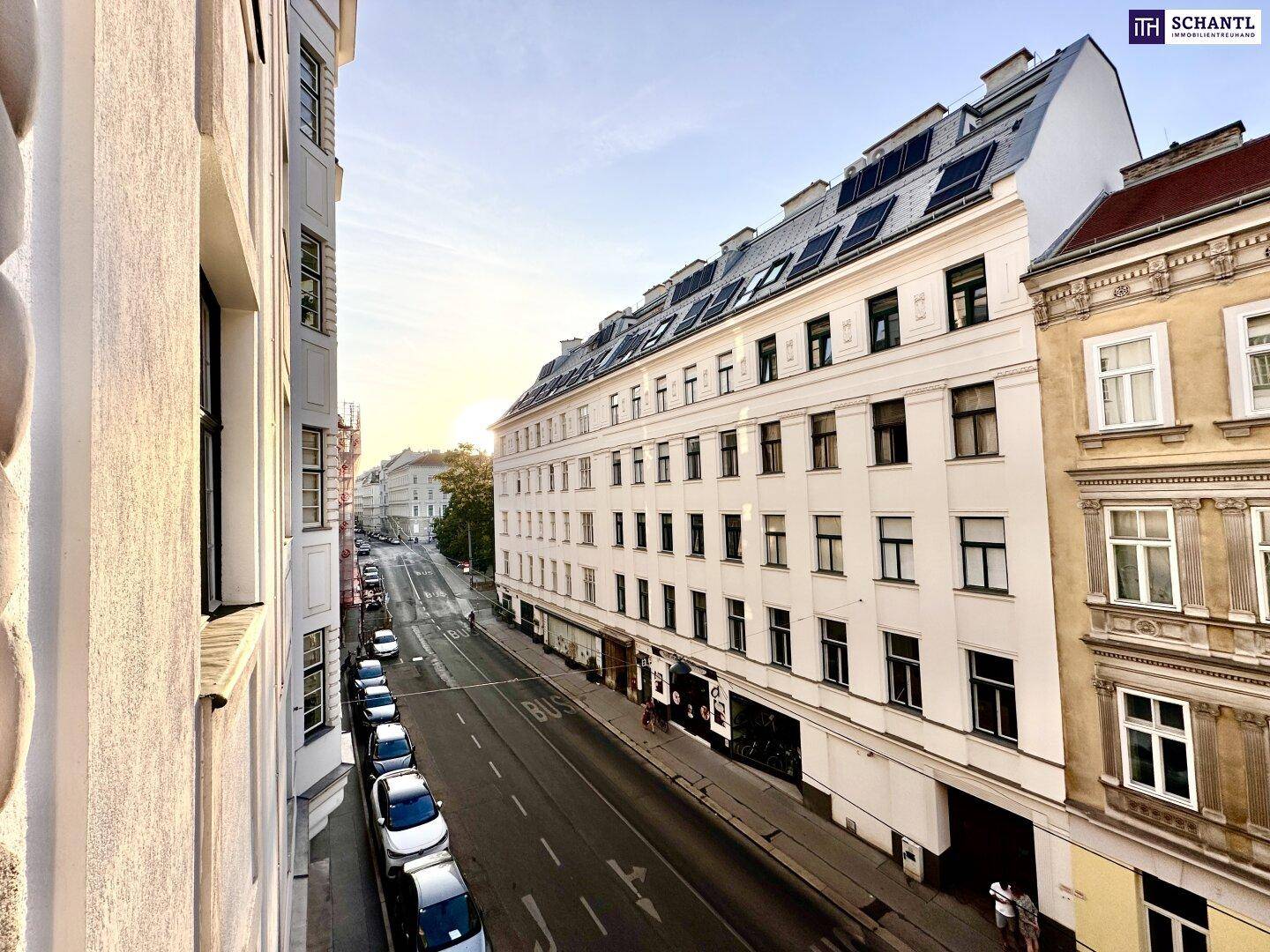 Weitblick auf eine städtische Straße mit Gebäuden und parkenden Fahrzeugen bei Sonnenuntergang.