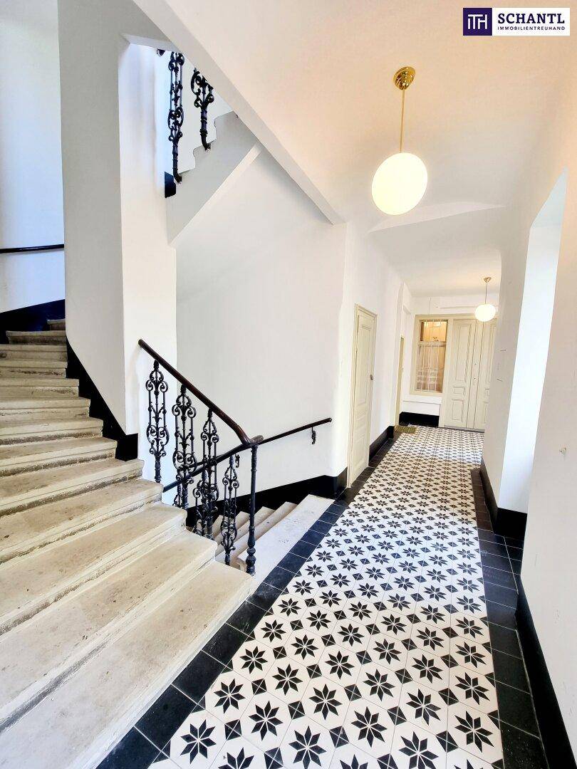 Eingangsbereich mit gemusterten Fliesen, Steintreppe und schmiedeeisernem Geländer in einem Altbau.