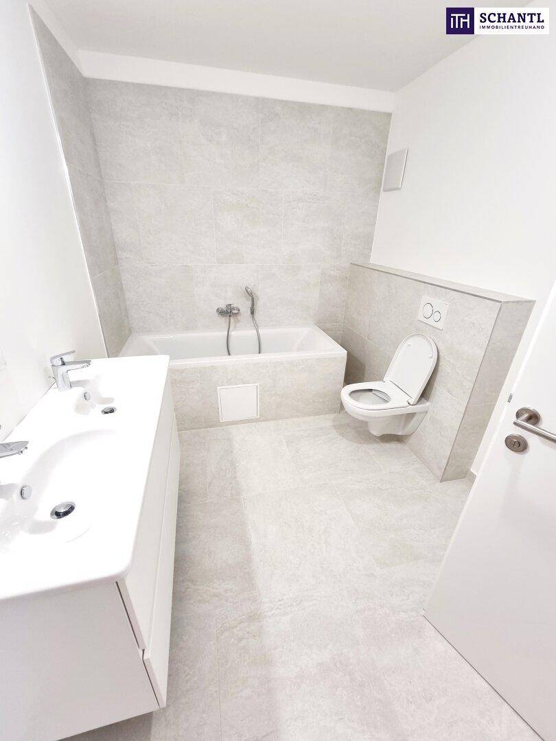 Modernes Badezimmer mit hellgrauen Fliesen, Badewanne, wandhängendem WC und Doppelwaschbecken.
