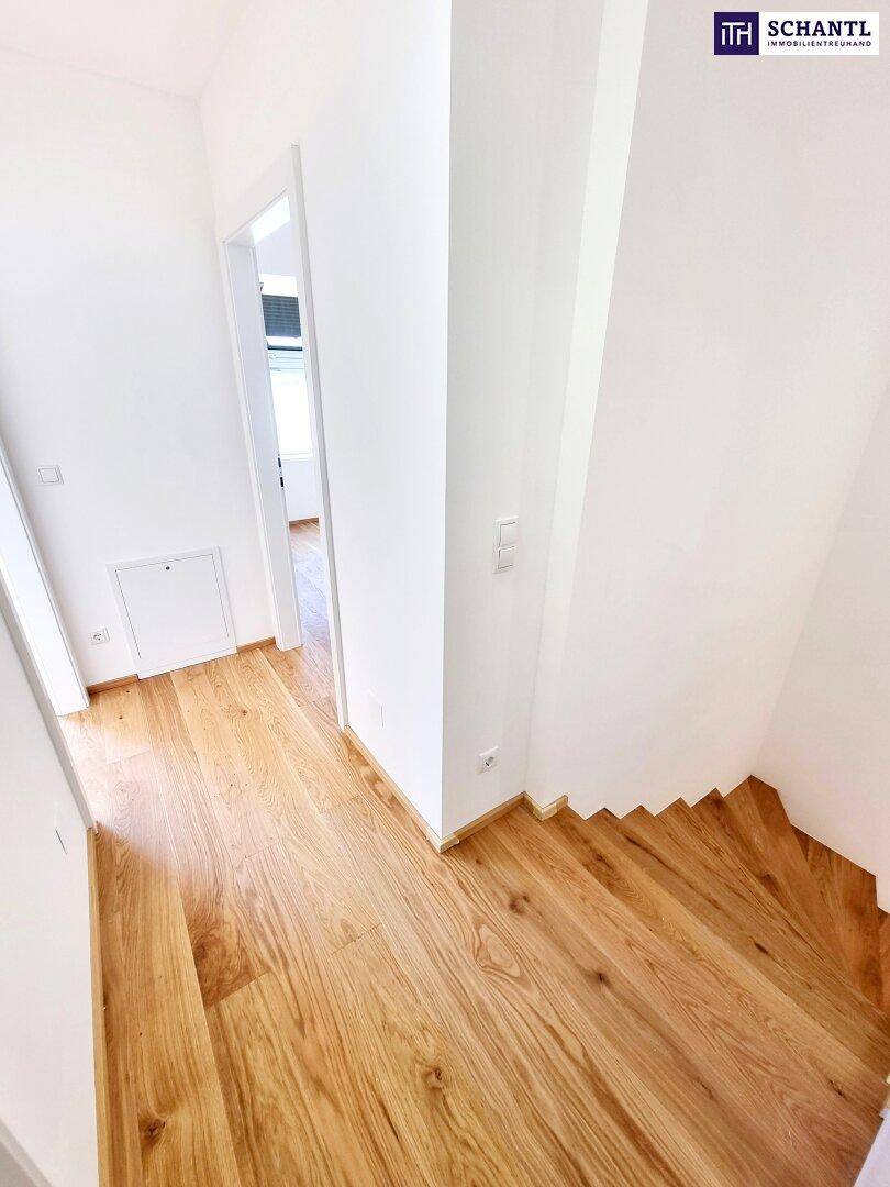 Heller Flur mit Holzparkettboden und einer eleganten Holztreppe, die in die obere Etage führt.