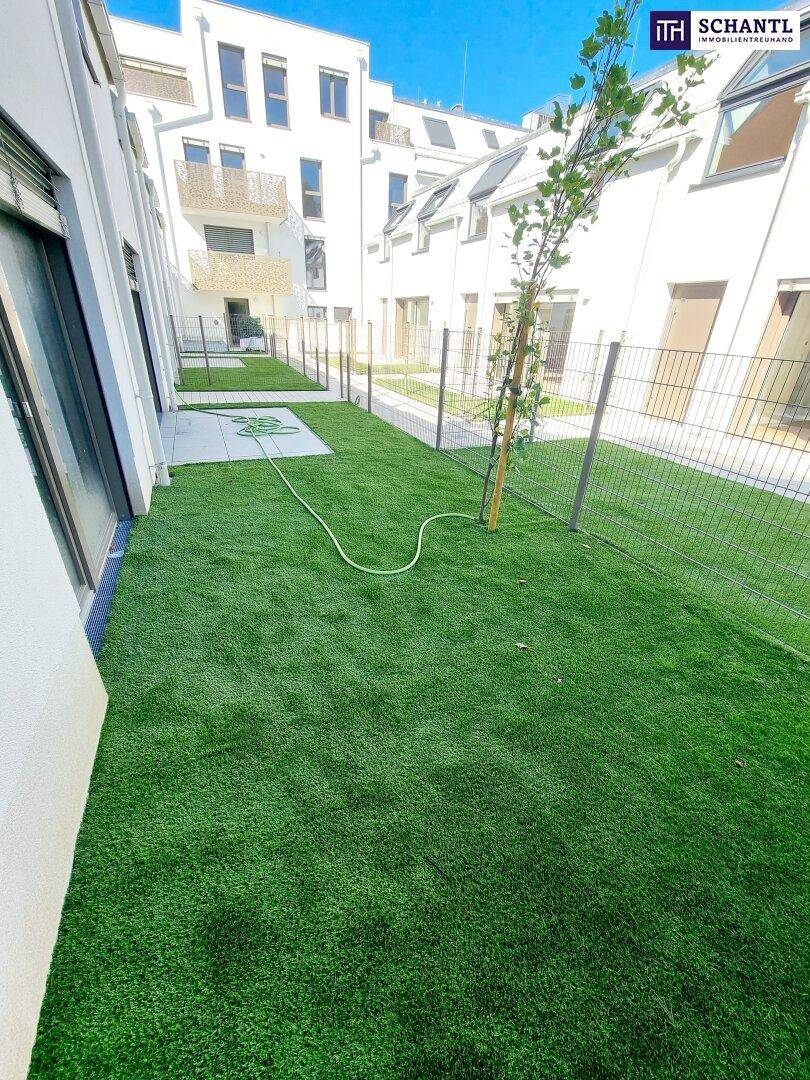 Kleiner privater Gartenbereich mit Kunstrasen und Zaun, umgeben von modernen Gebäuden.