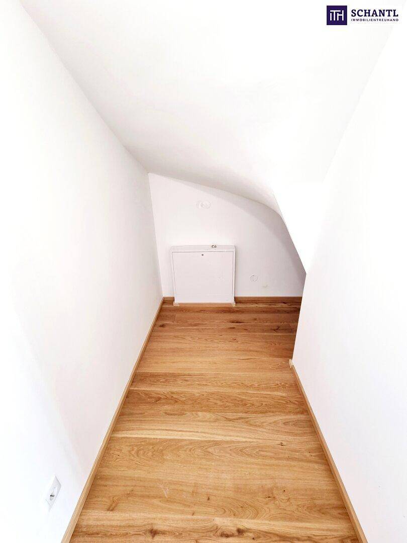Schmaler Flur im Dachgeschoss mit Holzparkett und weiß gestrichenen Wänden.