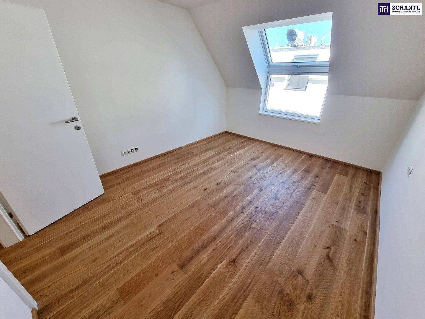 Dachgeschosszimmer mit Parkettboden, weiß gestrichenen Wänden und einem Dachfenster.