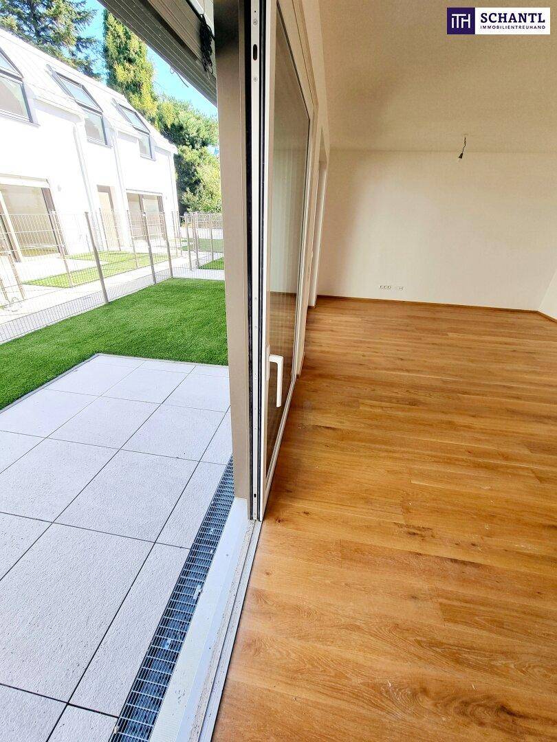 Blick aus dem Wohnzimmer auf die geflieste Terrasse und den grünen Gartenbereich durch große Schiebetüren.
