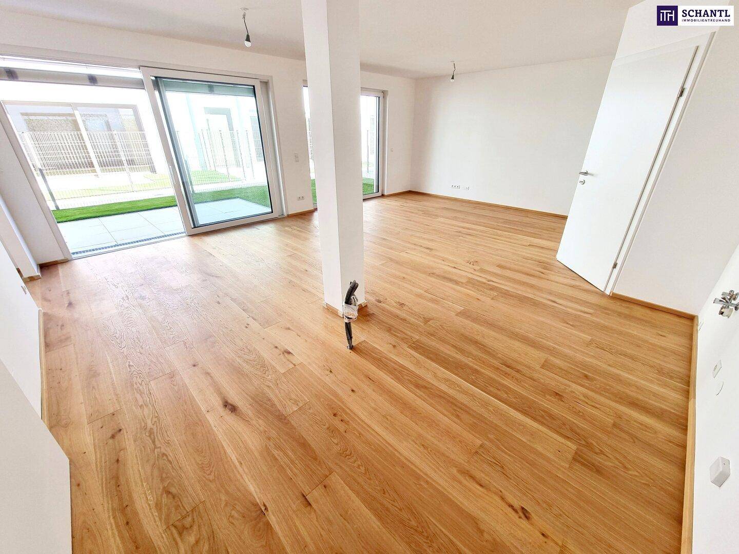 Heller Wohnbereich mit Eichenparkett und Zugang zu einer Terrasse mit Kunstrasenfläche.
