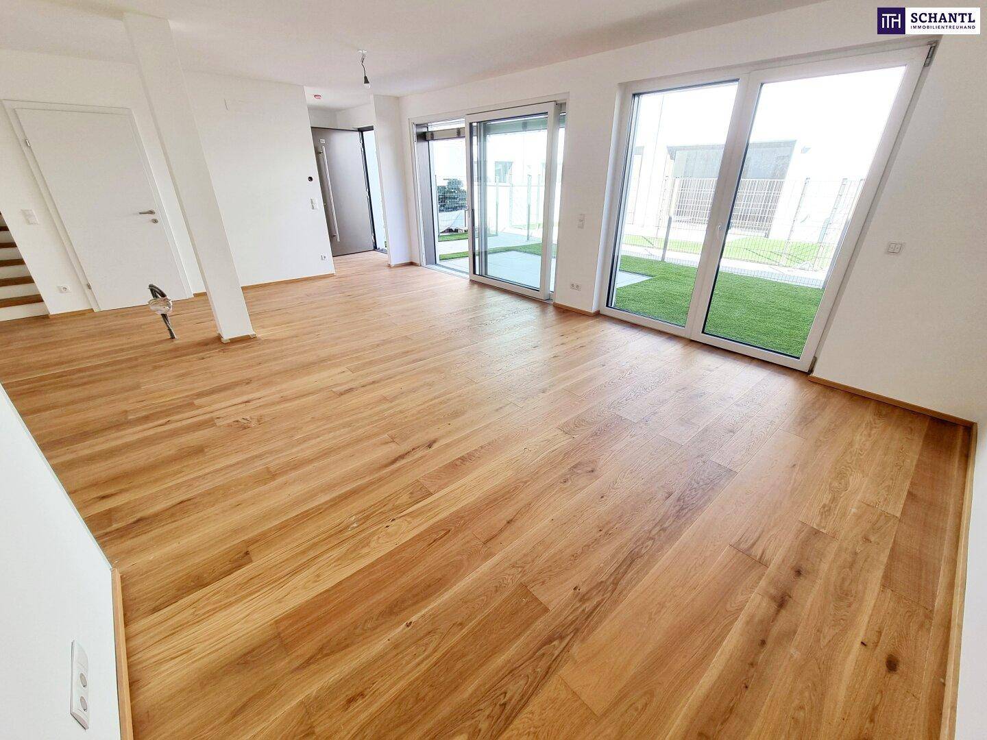 Geräumiger Wohnbereich mit hellem Parkettboden und großen Fenstern, die viel Licht hereinlassen.
