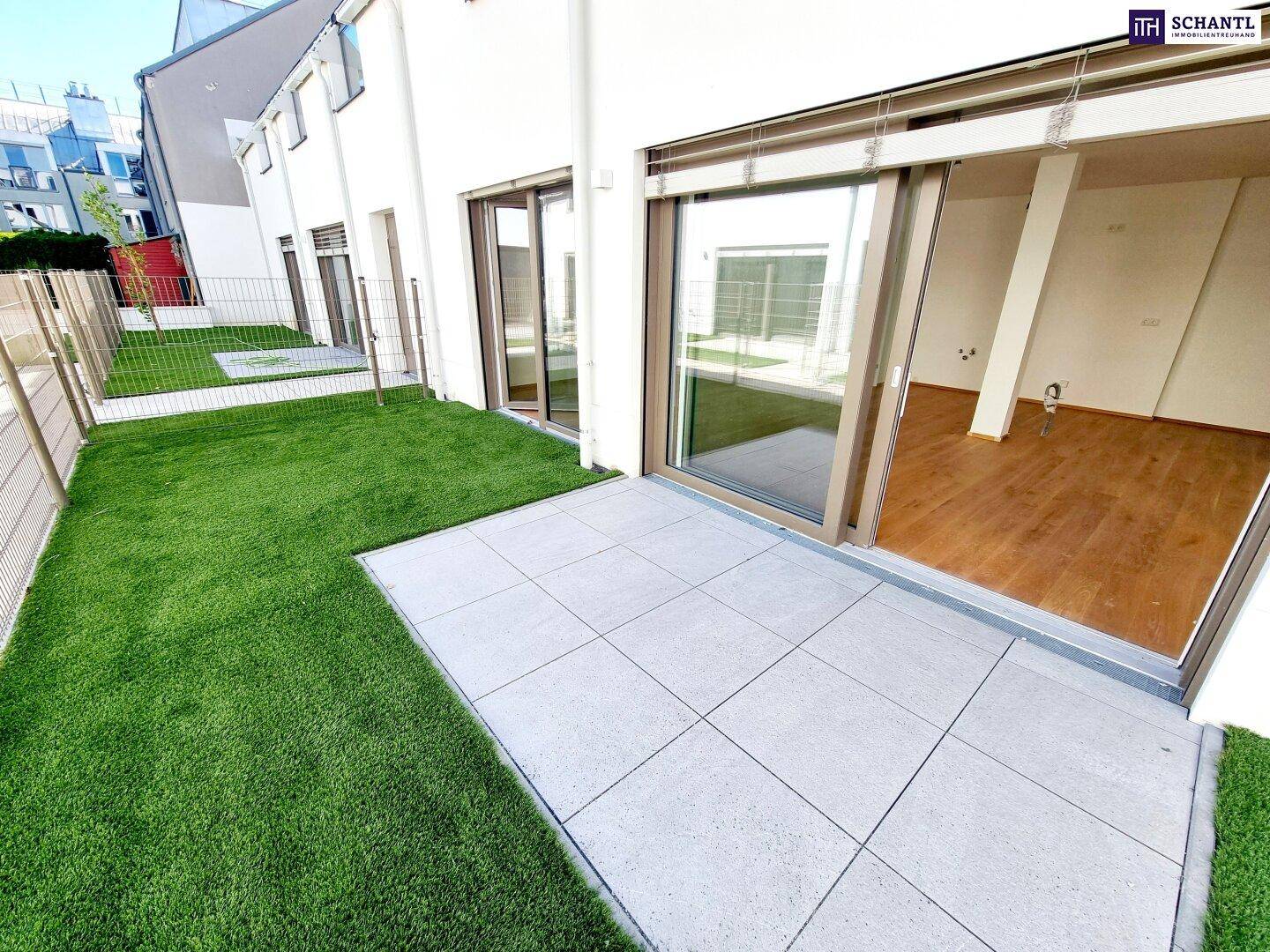 Gepflegter Gartenbereich mit Kunstrasen und gefliester Terrasse, direkt zugänglich vom Wohnraum.