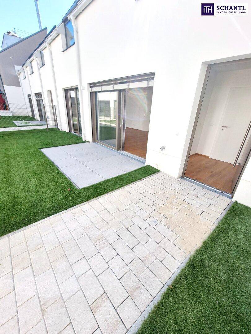 Außenbereich mit Kunstrasen, gepflasterter Terrasse und Zugang zu den Wohnräumen durch Glasschiebetüren.