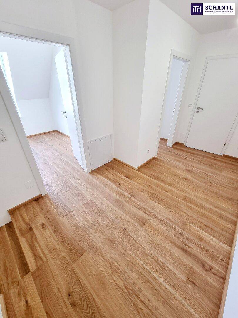 Flur mit hellem Parkettboden und Zugang zu einem Zimmer mit Dachschräge.