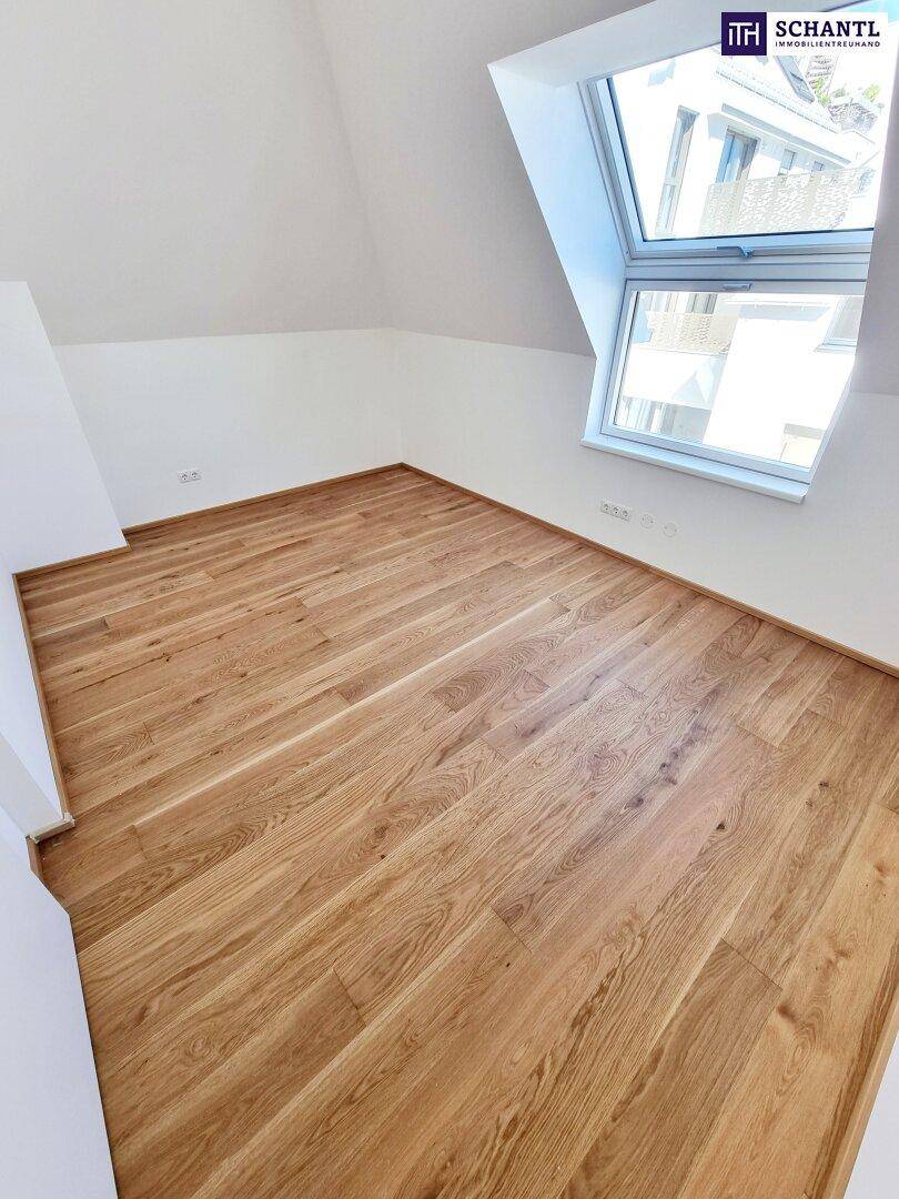 Helles Schlafzimmer im Dachgeschoss mit Parkettboden, weißen Wänden und einem großen Dachfenster.