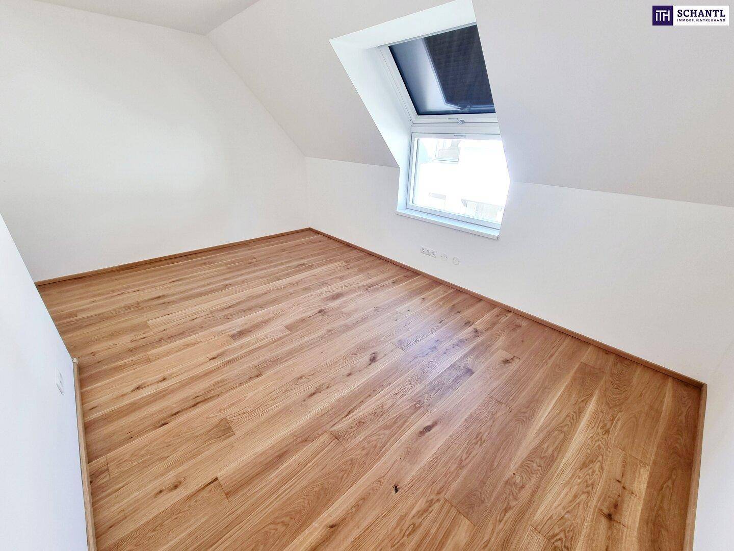 Dachgeschosszimmer mit hellem Parkettboden, weißen Wänden und einem schrägen Dachfenster.