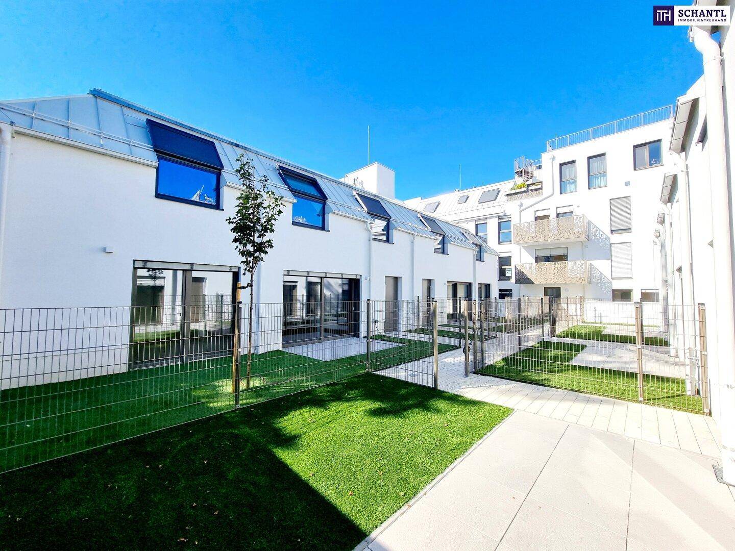 Gepflegter Gartenbereich mit Rasen und gepflasterten Wegen zwischen modernen Häusern.