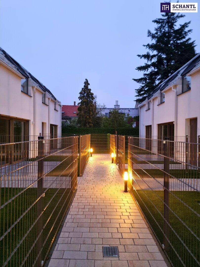Beleuchteter Weg zwischen modernen Gebäuden bei Dämmerung mit Gartenbeleuchtung.