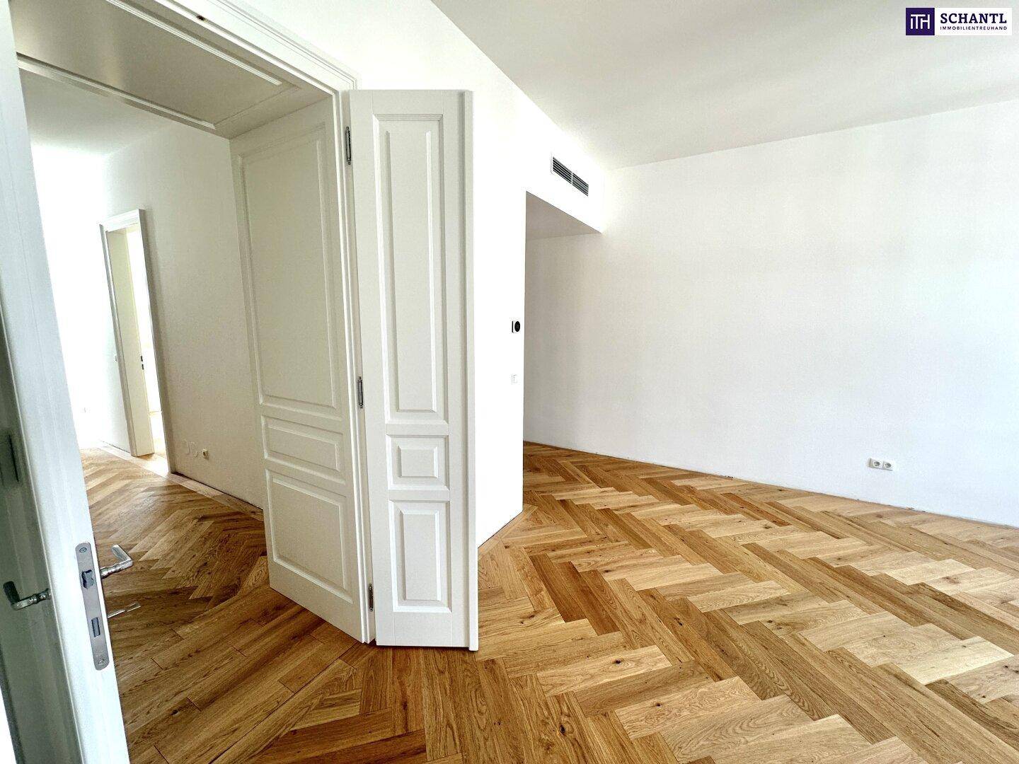 Geräumiger, leerer Raum mit elegantem Fischgrätparkett und hohen weißen Türen, die zu weiteren Zimmern führen.