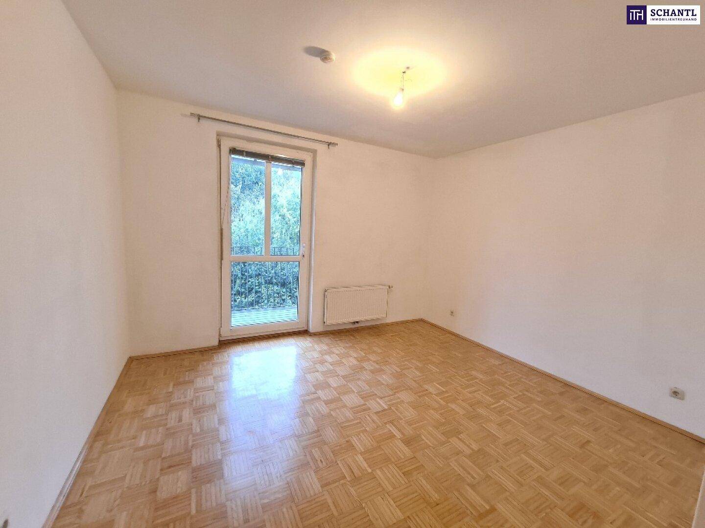 Helles Schlafzimmer mit Parkettboden und großem Fenster mit Blick ins Grüne.