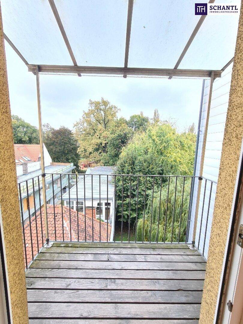 Kleiner Balkon mit Holzboden und Blick ins Grüne sowie auf umliegende Dächer.