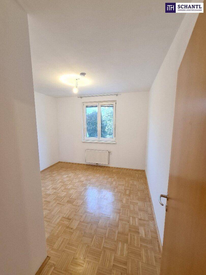 Helles Zimmer mit Parkettboden und Fenster, das viel natürliches Licht hereinlässt.