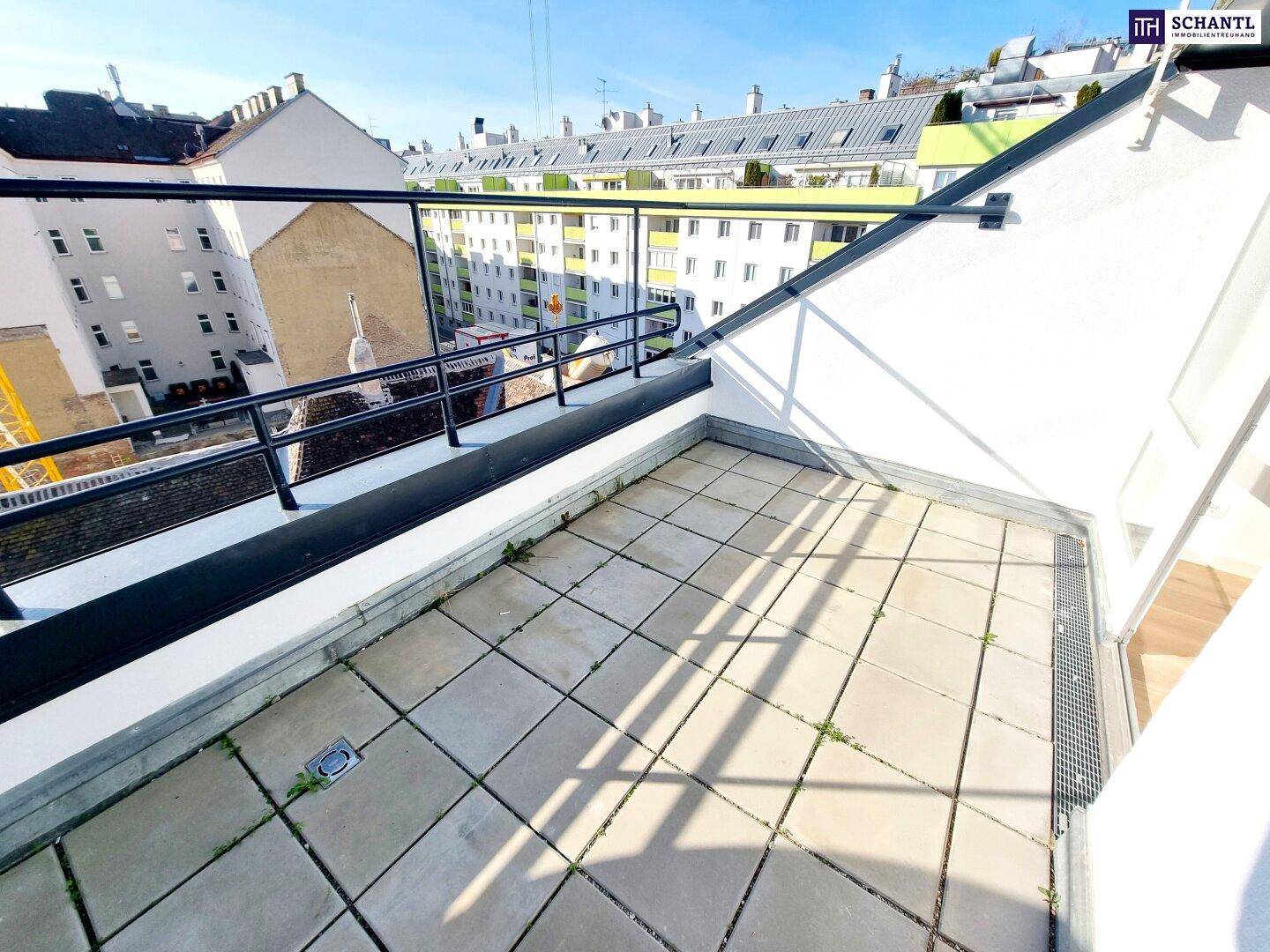Kleiner Balkon mit Fliesenboden und Blick auf die umliegenden Gebäude unter blauem Himmel.