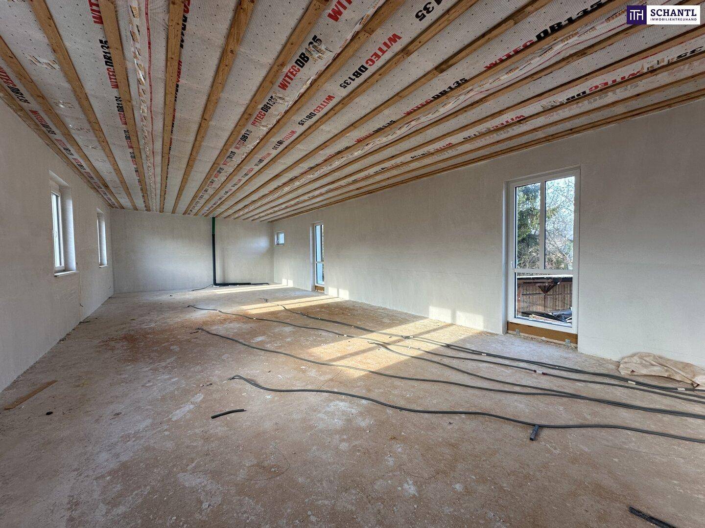 Heller Rohbau-Raum mit Holzbalkendecke, Betonboden und viel Sonnenlicht, bereit für den Ausbau.