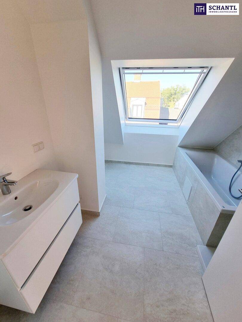 Modernes Badezimmer im Dachgeschoss mit Badewanne, Waschtisch und Dachfenster.