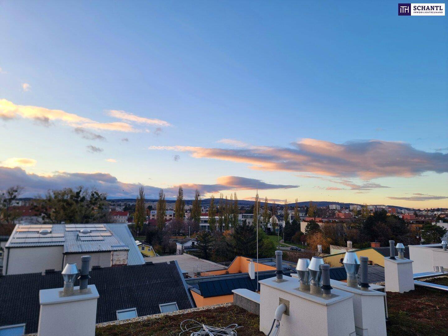 Panoramablick über die Stadt bei Sonnenuntergang mit Bergen im Hintergrund und Wohngebäuden.
